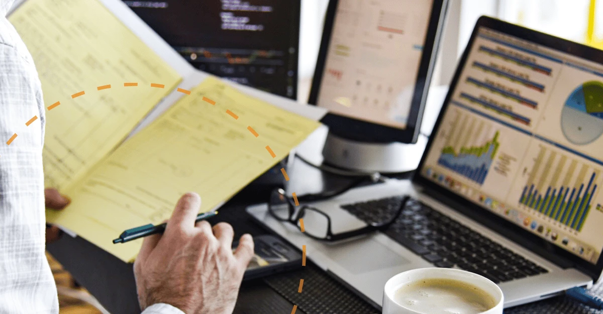 Reviewing paperwork beside a laptop displaying financial charts