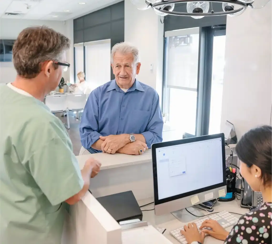 Older patient checking in at a clinic front desk with staff