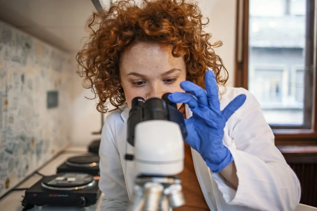 Laboratory scientist in blue gloves looking through a microscope