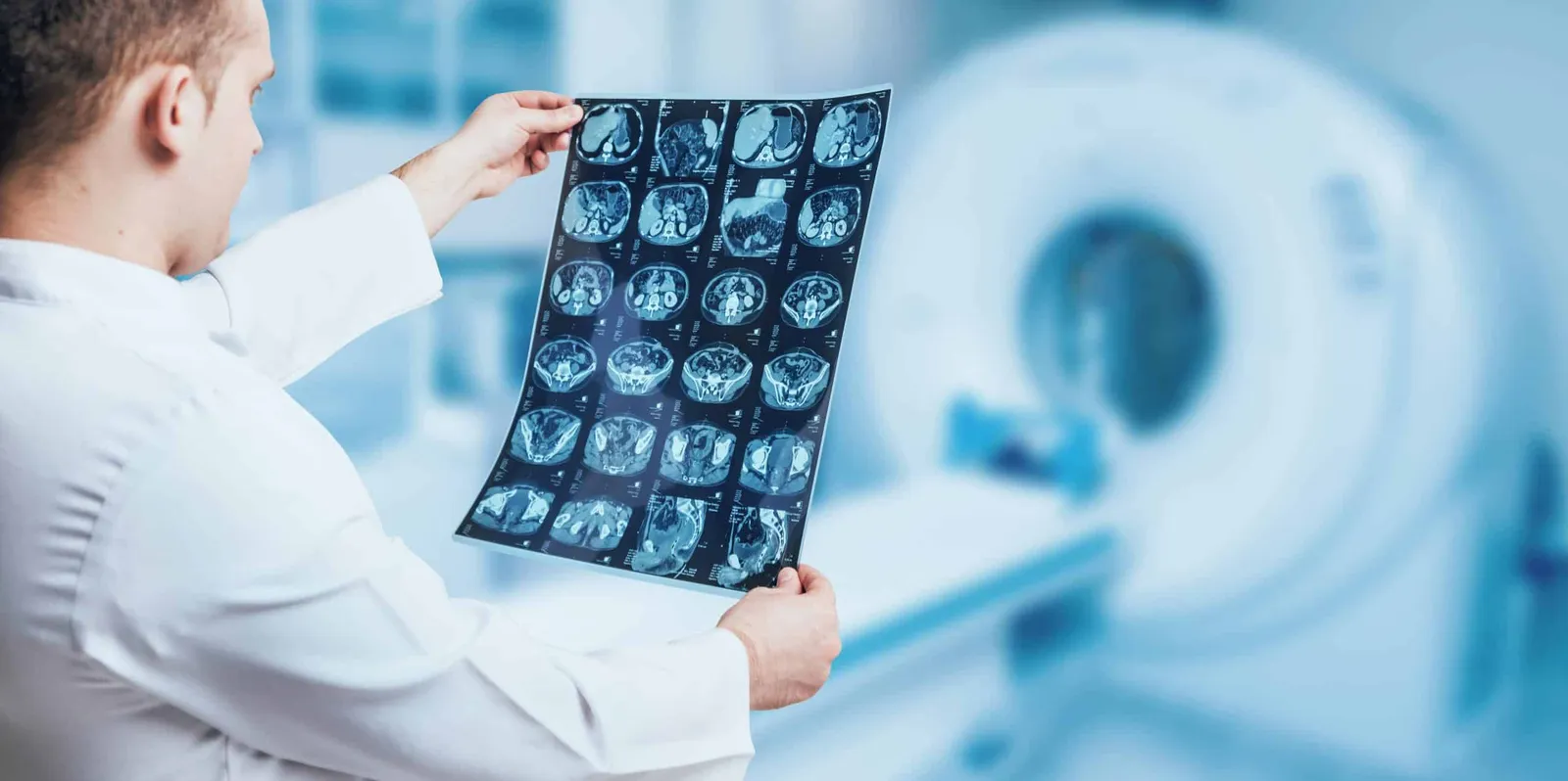 Physician reviewing a sheet of CT scan images in front of a CT scanner