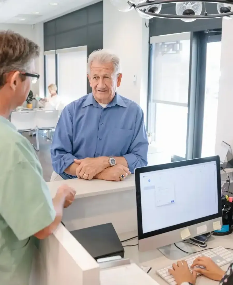 Older patient checking in at a clinic front desk with staff
