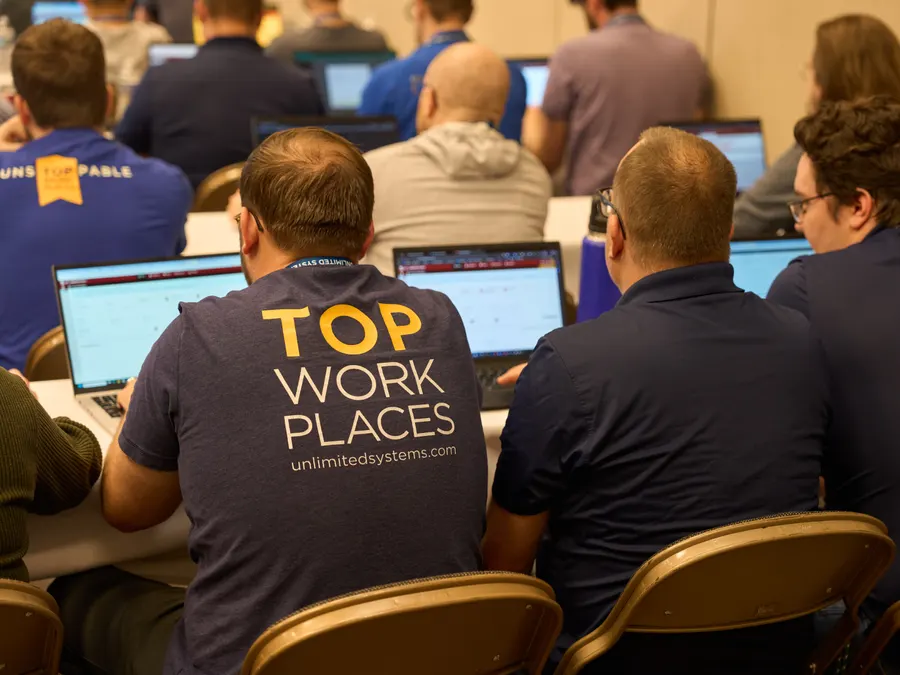 Unlimited Systems team members in Top Workplaces shirts working on laptops
