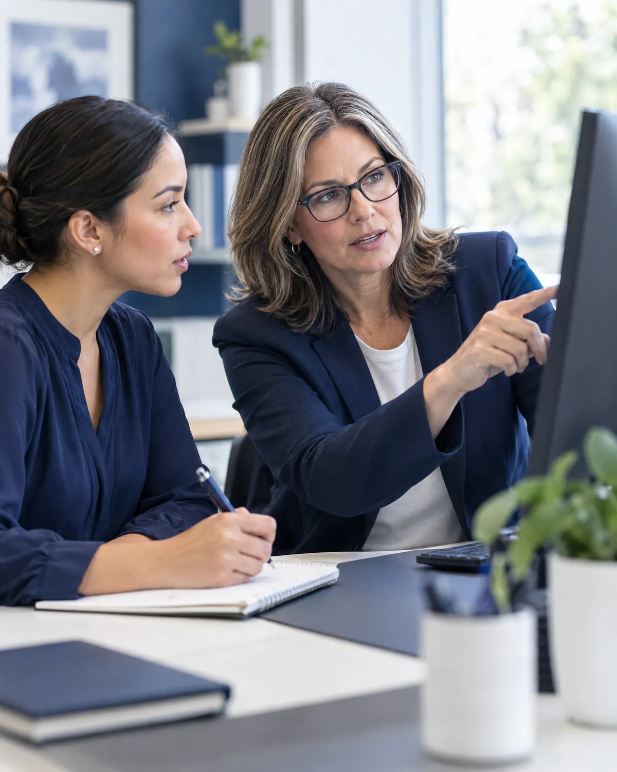 A/R team lead pointing at a monitor while a colleague takes notes
