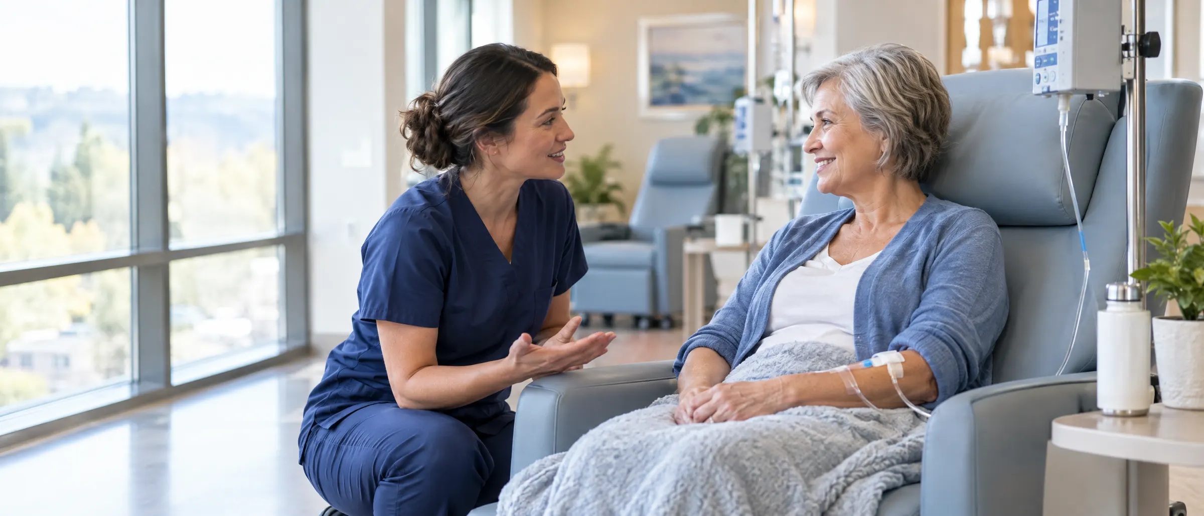 Infusion nurse kneeling to talk with a smiling patient in an infusion chair